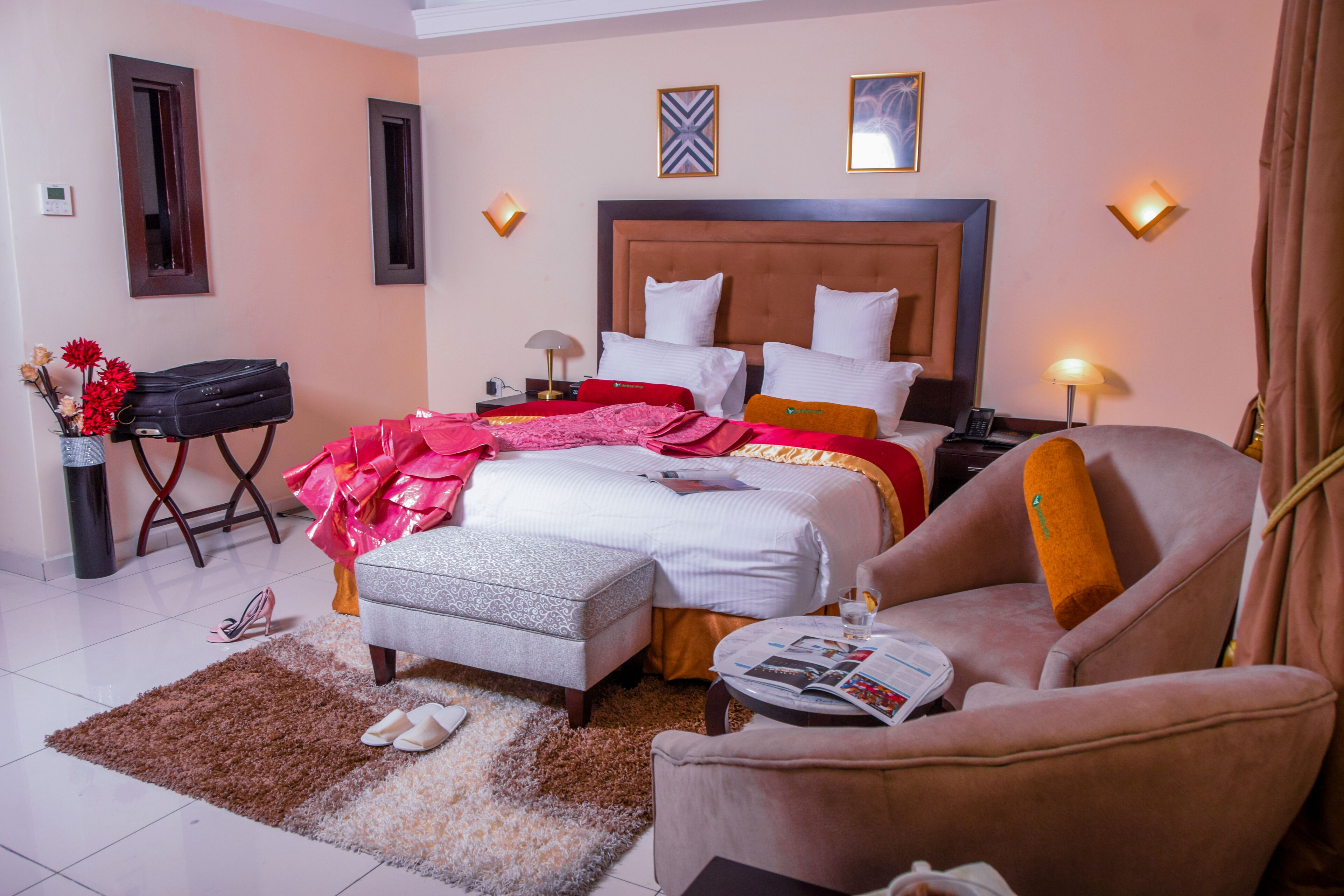 A hotel room with a large bed, a sitting area with a chair, a small table, and a bedside table with lamps.