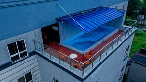 Ein Pool auf dem Dach mit blauem Baldachin, einer Glasbrüstung und einer kleinen Sitzecke mit Stühlen und einem Tisch.