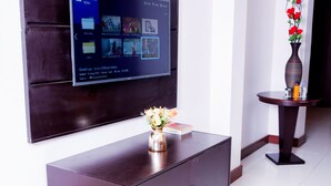 Ein modernes Interieur mit einem großen Flachbildfernseher an einer dunklen Wand, einer Holztische mit einer Blumenvase und einem kleinen runden Tisch mit einer Vase roter Blumen.