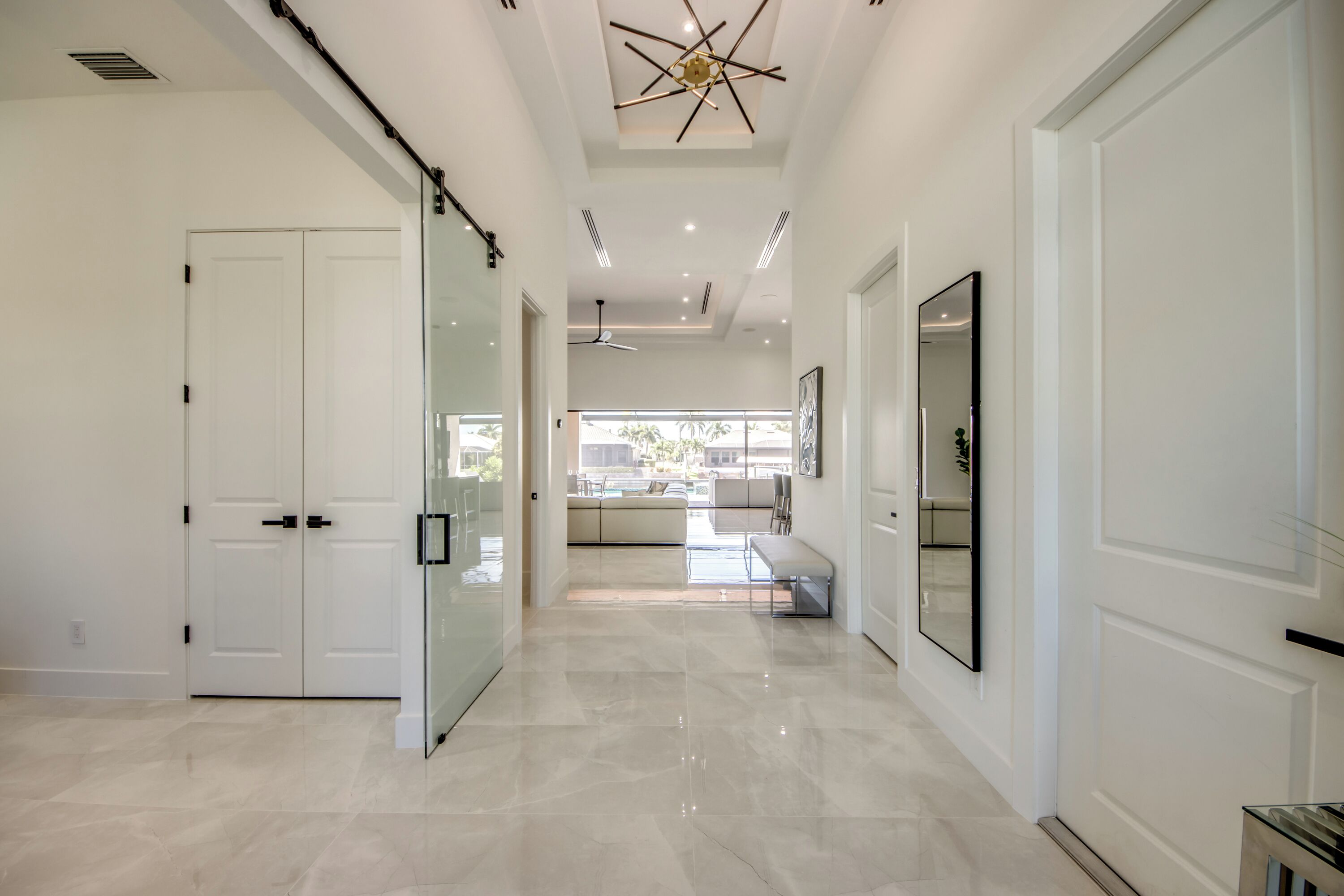 A modern hallway with a glass door, a ceiling fan, and a bench.