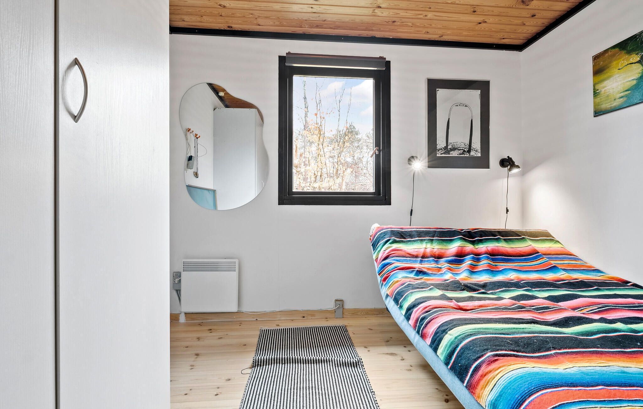 Un dormitorio con cama, espejo, ventana y radiador.