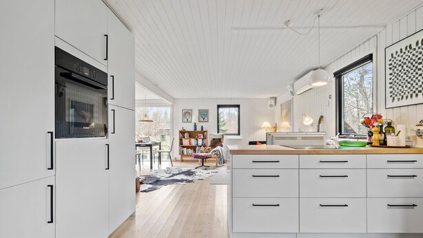 A modern kitchen with white cabinetry, a central island, and a dining area with a view. - 3 bedroom nice home in Vig (Vig)