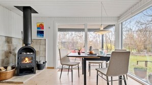 A modern kitchen with a wood-burning stove, a dining area with chairs and a table, and large windows offering a view of the outdoors. - 3 bedroom nice home in Vig (Vig)