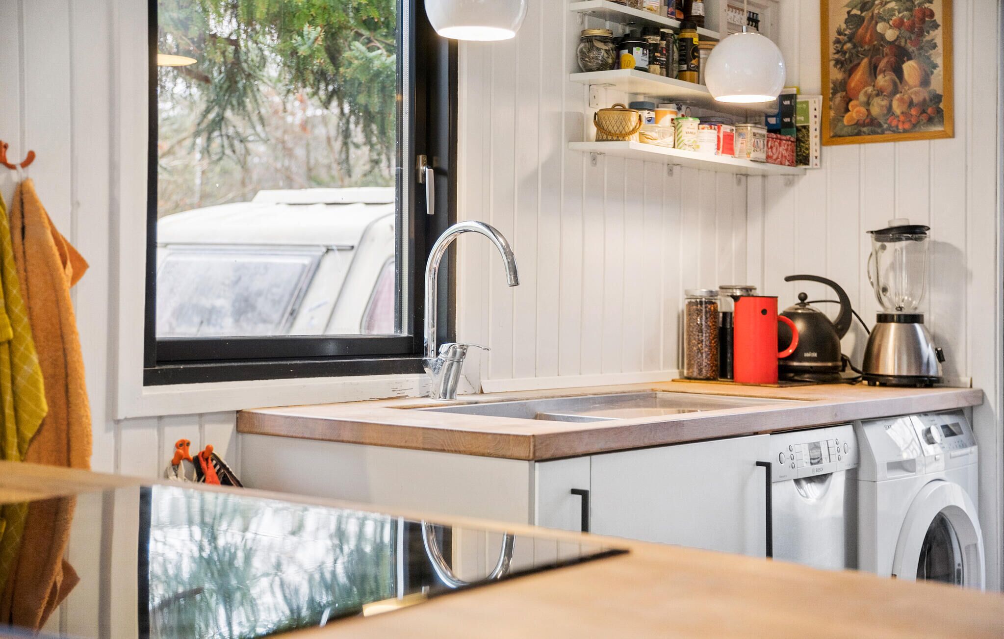 A modern kitchen with a large window, a sink, a kettle, a blender, and a washing machine.