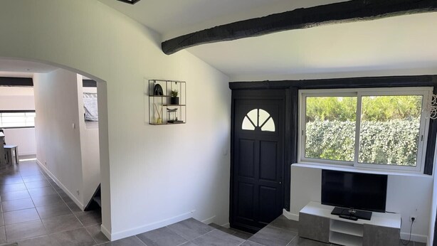 Un salon moderne avec un téléviseur, une porte noire et une fenêtre donnant sur un espace verdoyant.