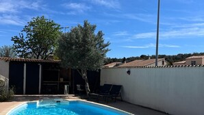 Une piscine à l’eau d’un bleu limpide, entourée d’un petit muret et de quelques arbres.