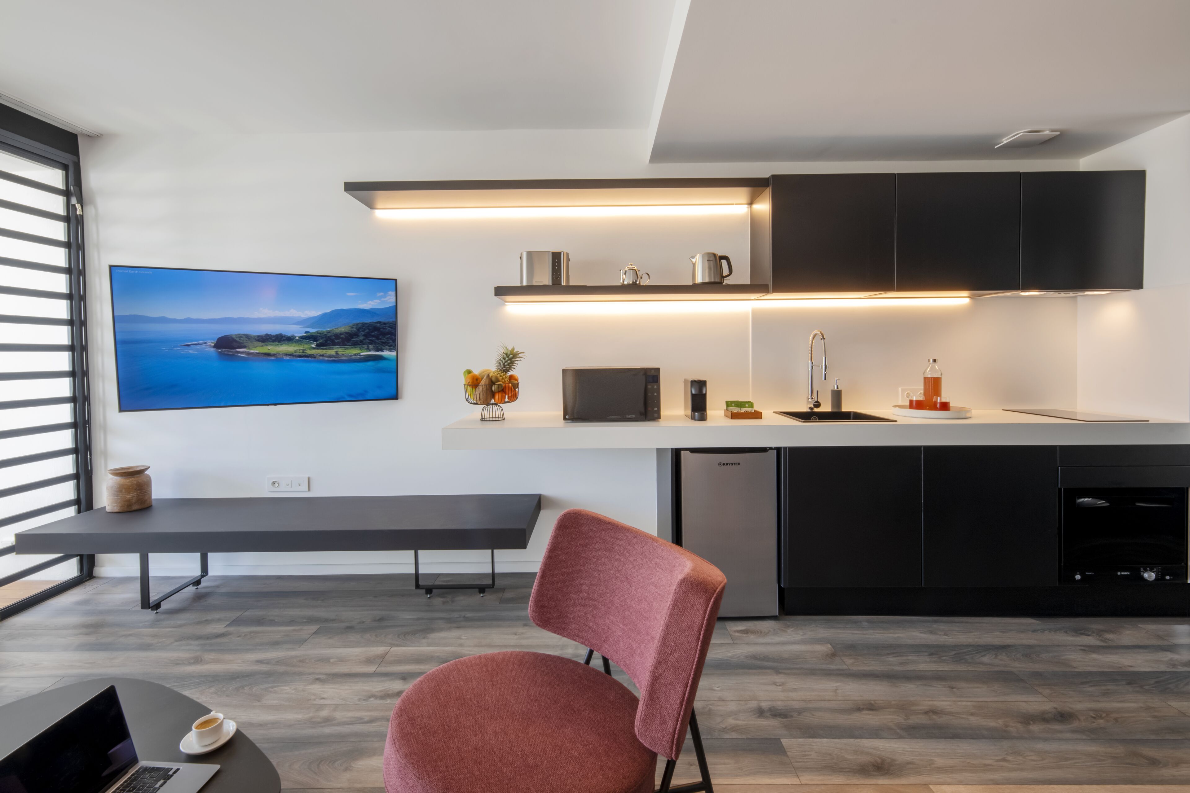 Una cocina moderna con televisión de pantalla plana, una mesa de comedor y una silla roja.