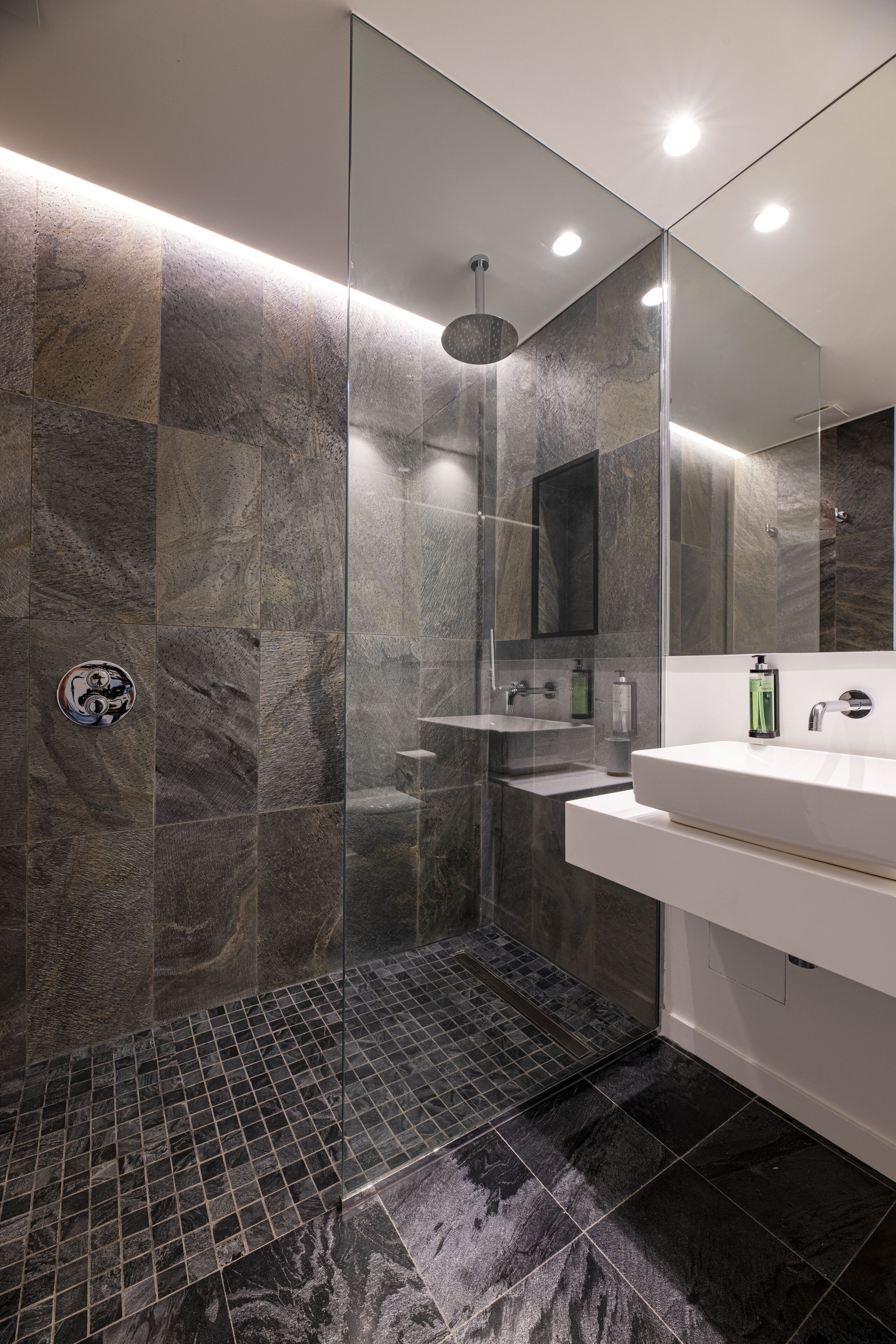 Un baño moderno con ducha envuelta en vidrio, un lavabo blanco y un espejo grande.