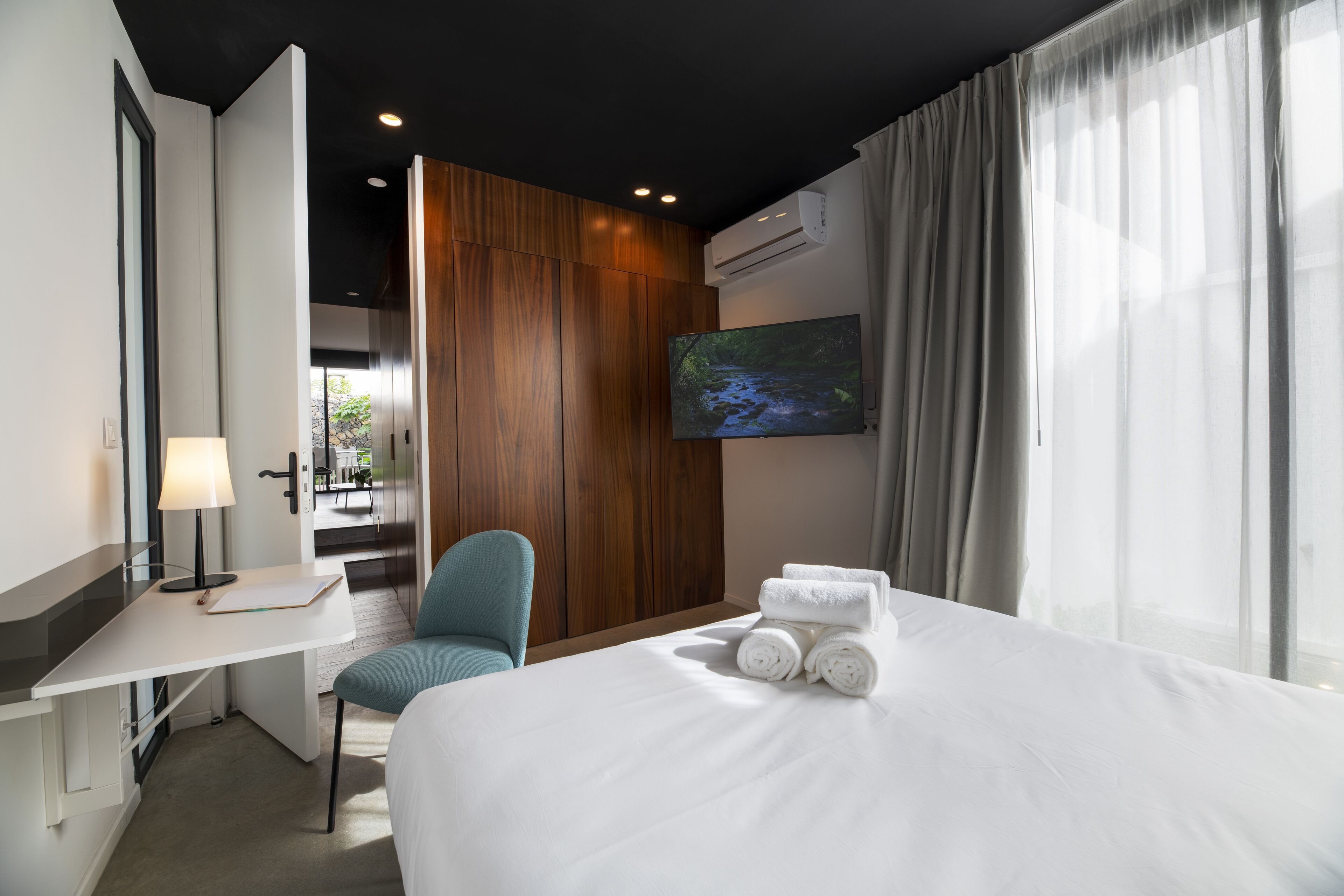 Una habitación de hotel con cama, escritorio, silla, televisor y ventana con cortinas.
