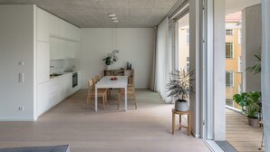 A modern kitchen with white cabinets, a dining area with a white table and wooden chairs, and a potted plant. - Wilmina Apartments & Lofts (Berlin)