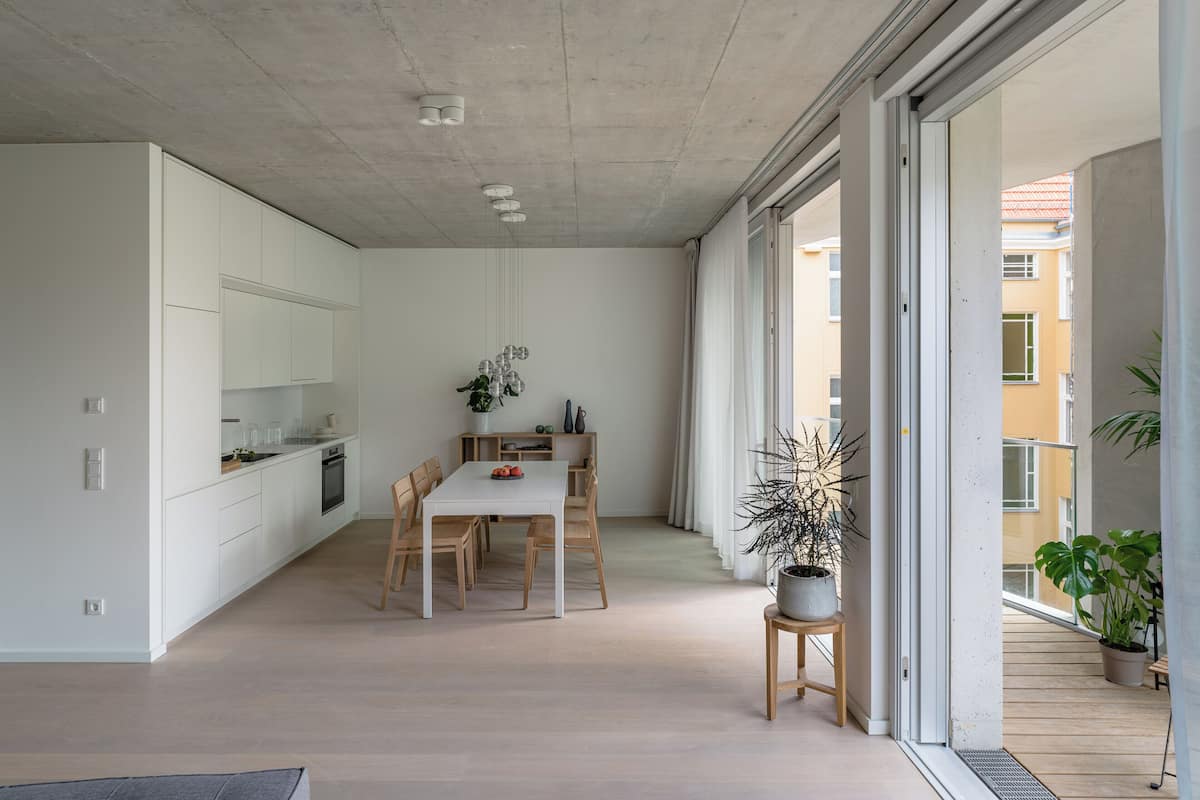 A modern kitchen with white cabinets, a dining area with a white table and wooden chairs, and a potted plant.