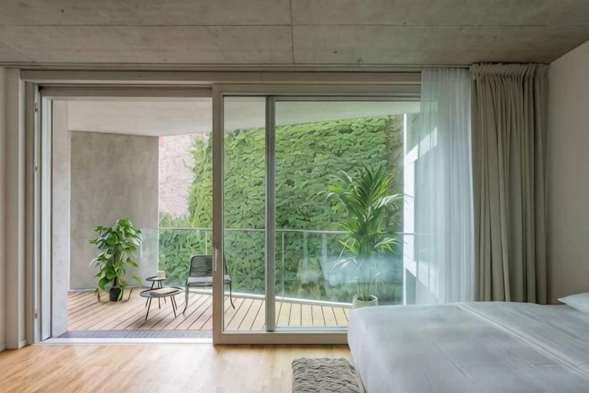 A bedroom with a large sliding glass door leading to an outdoor balcony with a view of greenery.