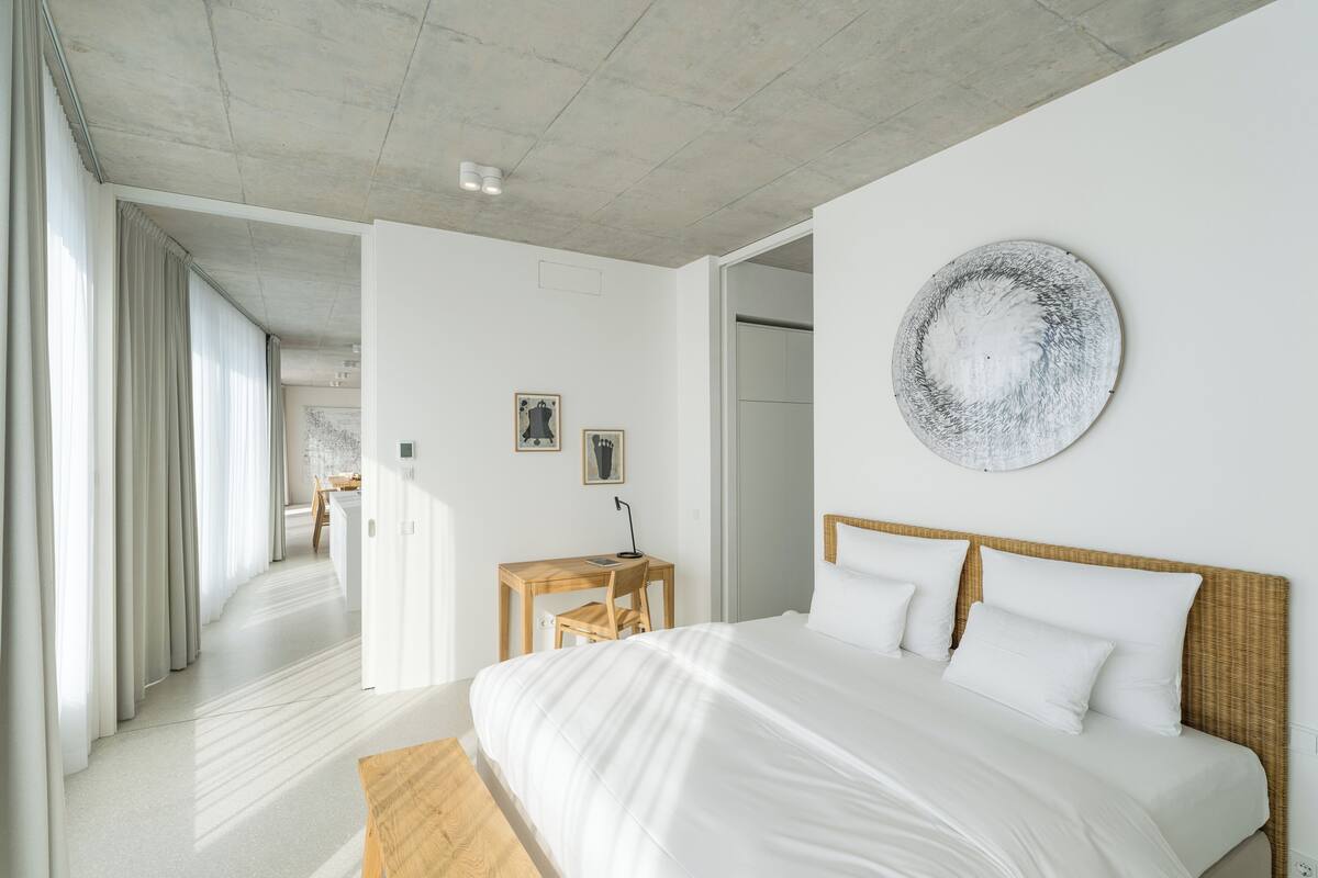 A modern bedroom with a large bed, a wooden desk, and a round artwork on the wall.