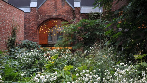 A brick building with a large arched entrance, surrounded by dense foliage and white flowers. - Wilmina Apartments & Lofts (Berlin)