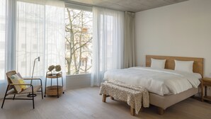 A bedroom with a large bed, a chair, a small table with a plant, and a window with sheer curtains. - Wilmina Apartments & Lofts (Berlin)