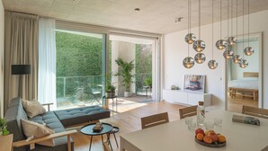 A modern living room with a sofa, dining table, and a large window. - Wilmina Apartments & Lofts (Berlin)