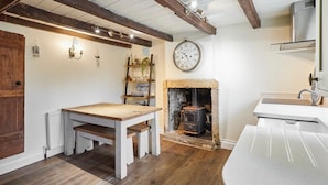 A rustic kitchen with a wooden table, a stone fireplace, a clock, and a white sink. - Host & Stay | Colcott Cottage (Fylingthorpe)