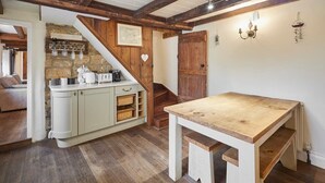A rustic kitchen with wooden beams, a white table, and a stone wall. - Host & Stay | Colcott Cottage (Fylingthorpe)