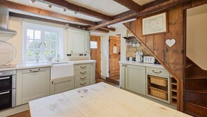 A kitchen with wooden beams, a large table, and cabinets. - Host & Stay | Colcott Cottage (Fylingthorpe)