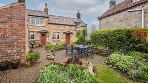 A courtyard with a stone building, a wooden bench, and a table with chairs. - Host & Stay | Colcott Cottage (Fylingthorpe)