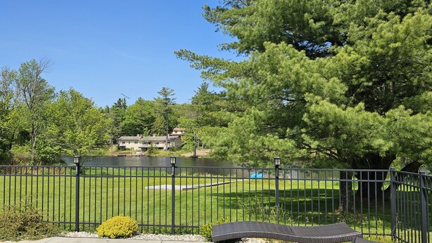 A fenced park with a lake, trees, and a house in the background. - Lakefront Escape -1 acre / private pool / kayak / fire pit / swing set (Blakeslee)