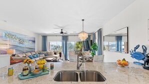 A modern kitchen with a large island, a sink, and a dining area with a sofa.