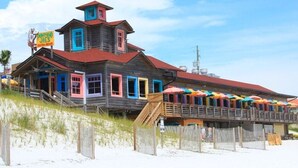 A wooden building with colorful doors and windows, a sign reading "Dompano Joe's," and a deck with umbrellas.