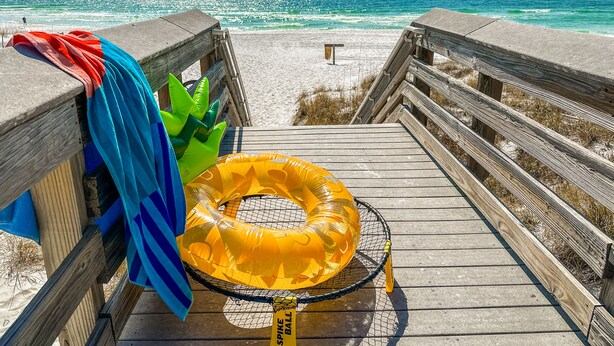 A wooden boardwalk leading to a sandy beach with a clear view of the ocean.