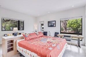 A bedroom with a large bed, a desk, and a chair. There are two windows with views of greenery. - The Cape 6031e1 1 Bedroom Home by RedAwning (Rockport)