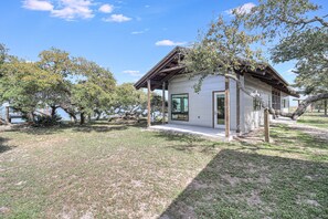 A small, single-story house with a covered porch, surrounded by trees and a grassy area. - The Cape 6031e1 1 Bedroom Home by RedAwning (Rockport)