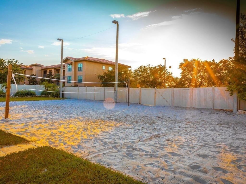 Un terrain de volleyball de sable avec un filet, entouré d’une petite clôture et avec un bâtiment en arrière-plan.