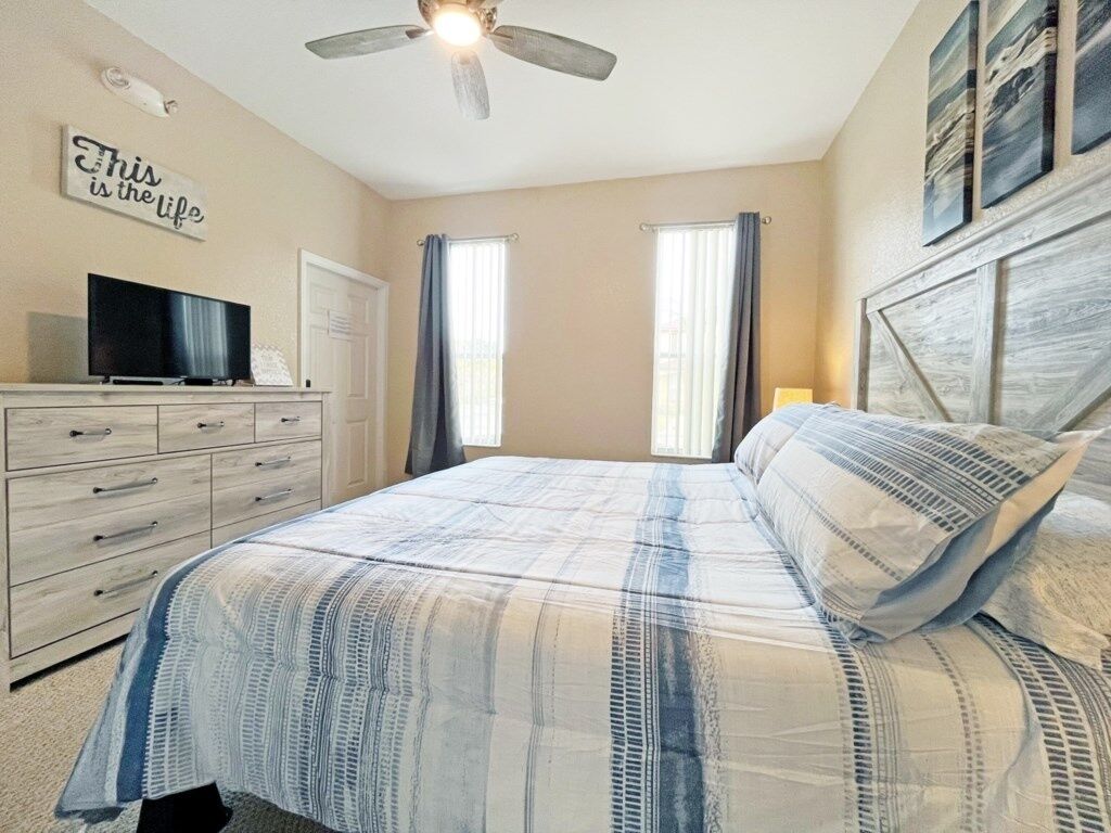 A bedroom with a bed, a dresser, a television, and a ceiling fan.