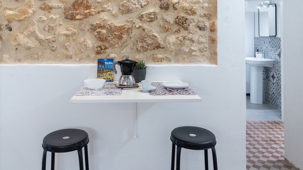 A kitchen with a stone wall, a coffee maker, a bowl, a cup, and a potted plant.