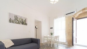 A modern living room with a grey sofa, a dining table with chairs, a patterned floor, and a door leading outside.
