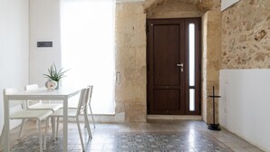 A dining area with a white table and chairs, a potted plant, and a door leading to a stone-walled room.