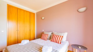 Une chambre à coucher avec un grand lit, une literie à rayures, deux oreillers, une table de chevet et une armoire en bois.