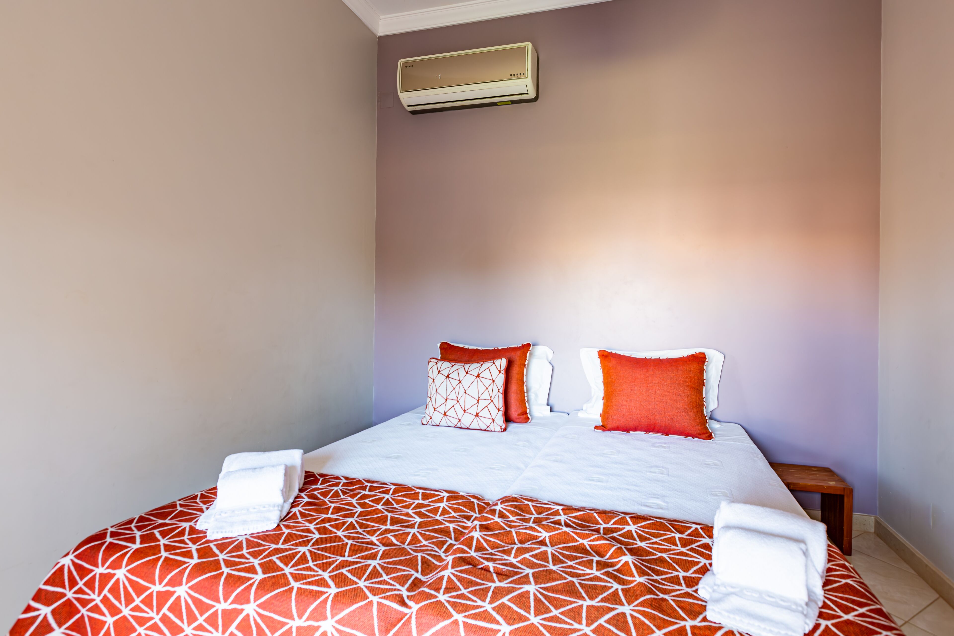 A neatly made bed with a patterned bedspread, two pillows, and a bedside table with a lamp.