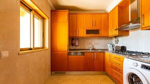 Une cuisine avec des meubles en bois, un lave-vaisselle, un lave-linge et une fenêtre avec des stores.