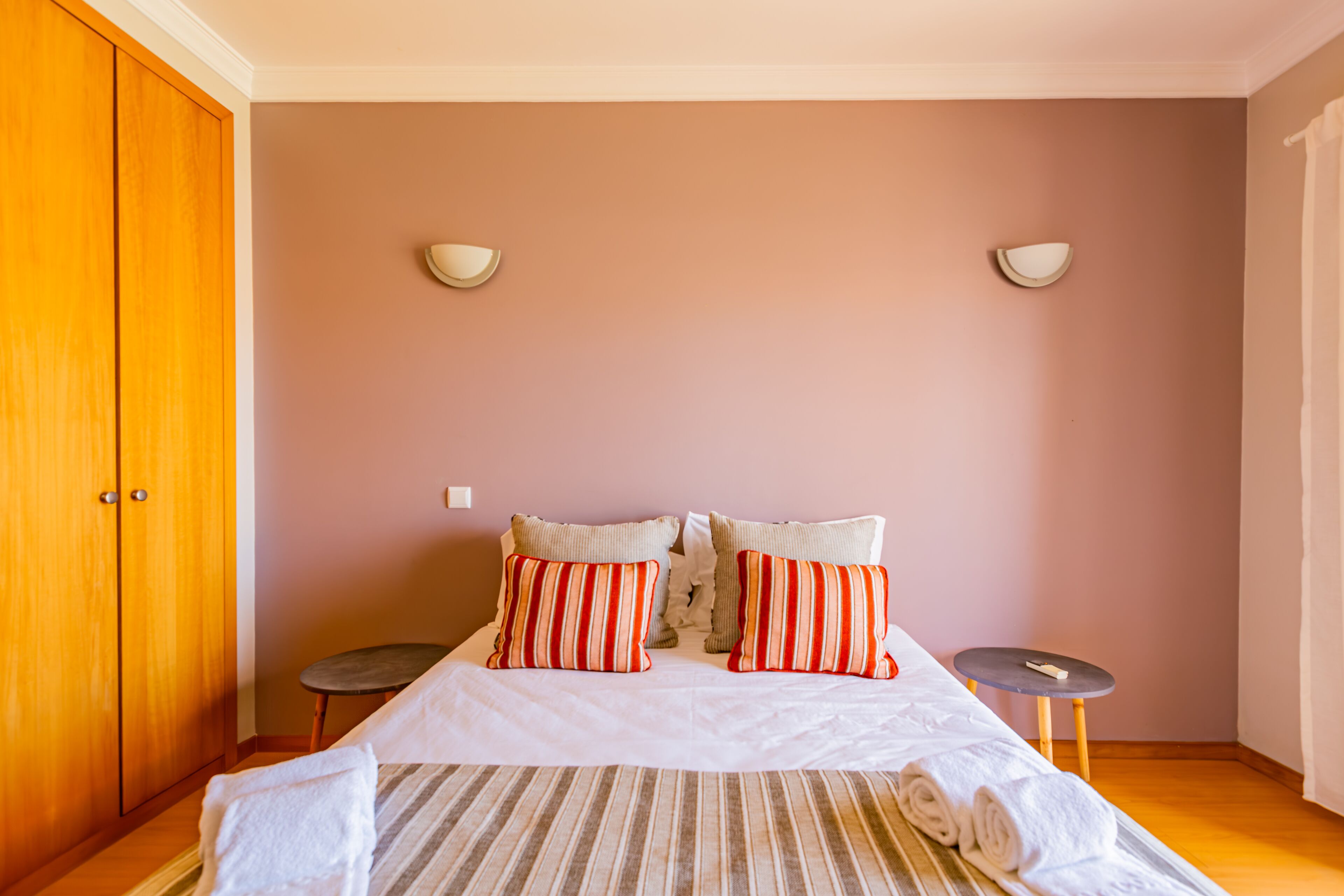 A bedroom with a bed, two bedside tables, a wardrobe, and two wall-mounted lights.
