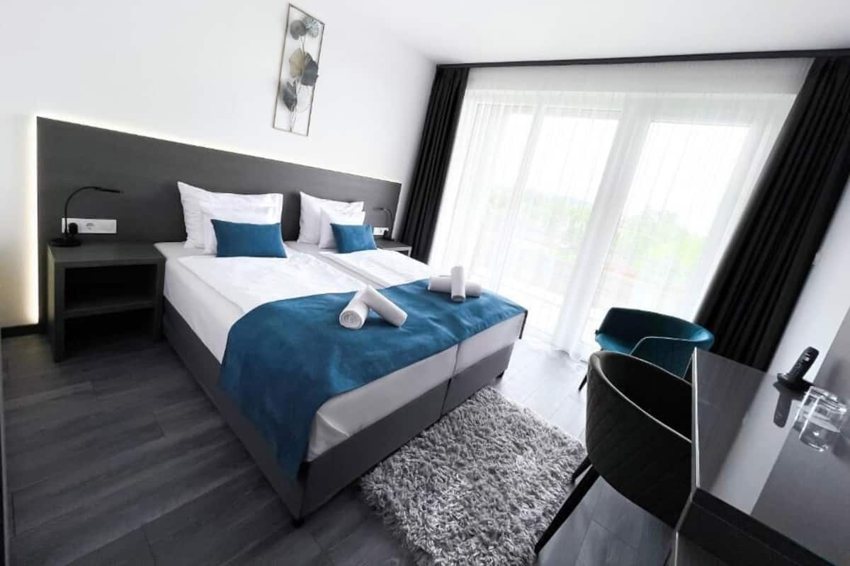 A modern hotel room with a large bed, a desk, and a view of the outdoors.