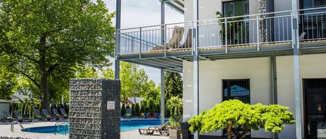 A modern multi-story building with a pool area, outdoor seating, and a well-maintained garden.