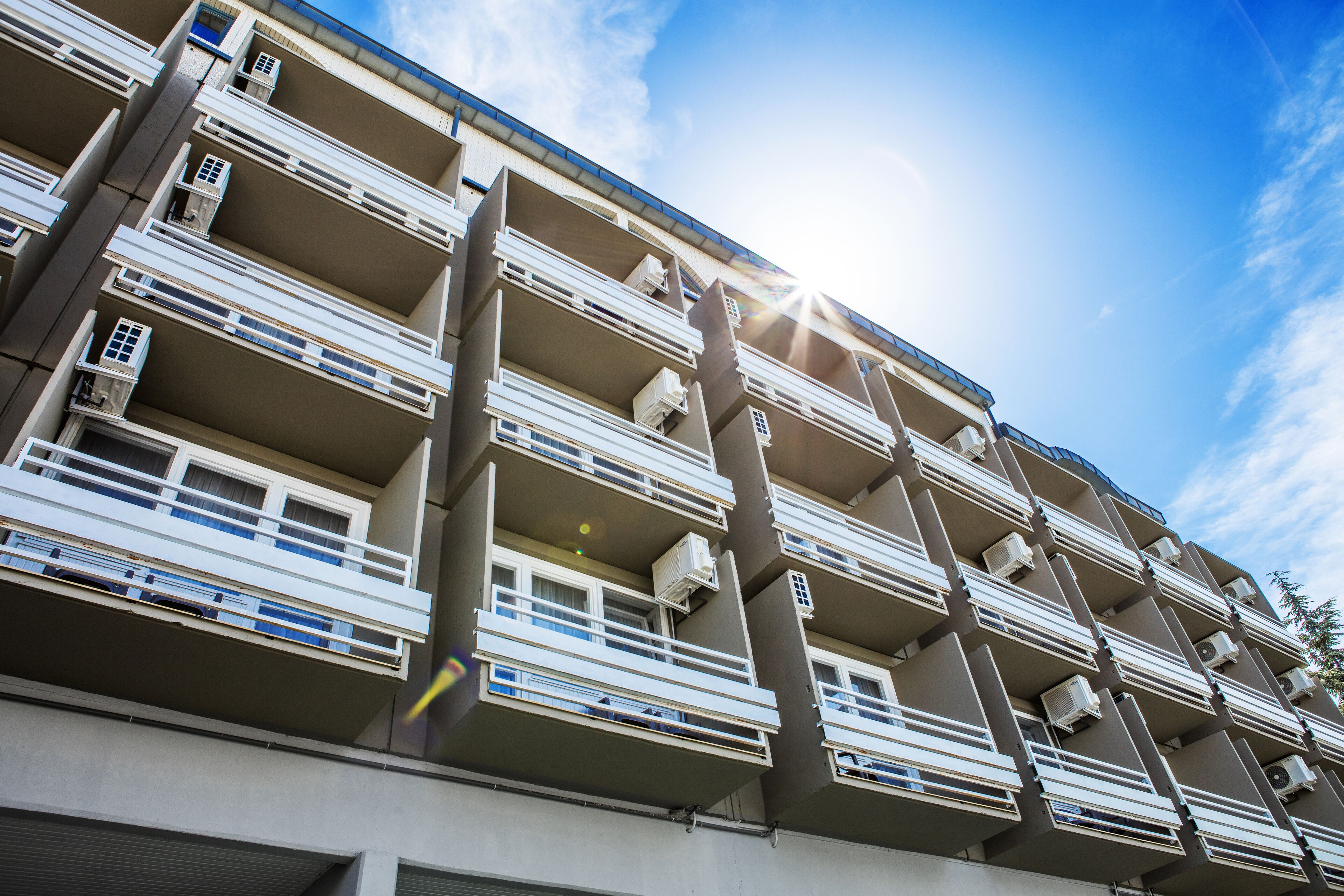 Un edificio residencial de varios pisos con balcones, unidades de aire acondicionado y un cielo despejado.