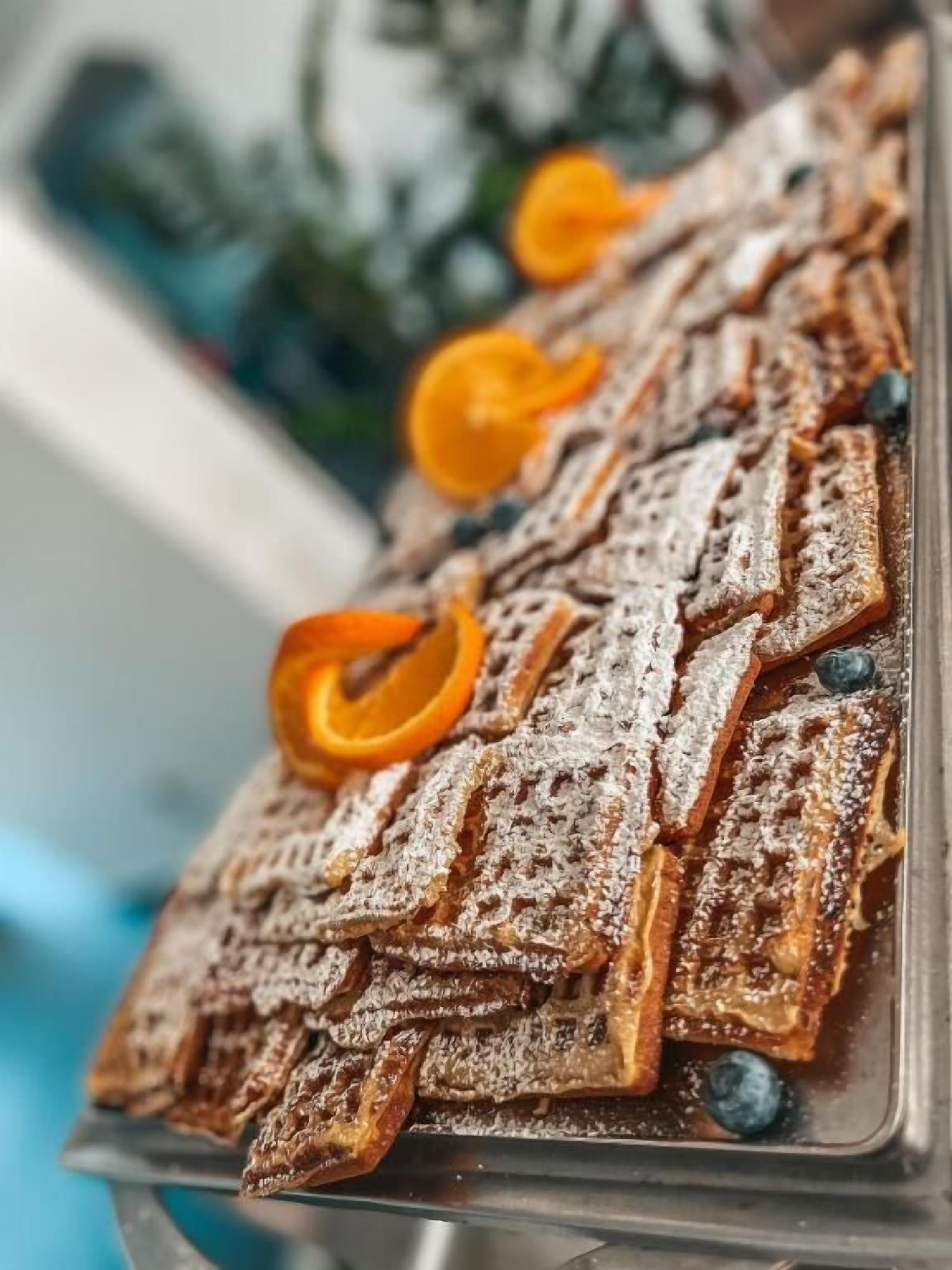 A tray of waffles with powdered sugar and orange zest garnish.