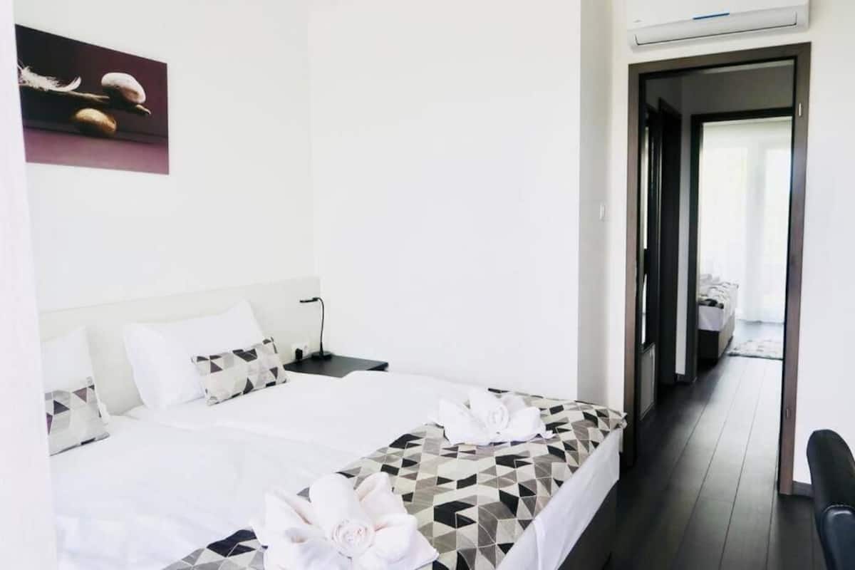 A hotel room with a bed, a desk, and a chair. There is a painting on the wall and a door leading to another room.
