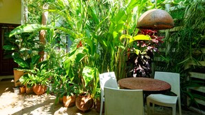 A patio area with a round table and two white chairs, surrounded by various potted plants and a rustic hanging lamp. - Hechtech House (Accra)