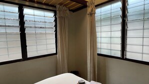 A hotel room with a bed, a window with blinds, a ceiling fan, and an air conditioning unit. - Hechtech House (Accra)