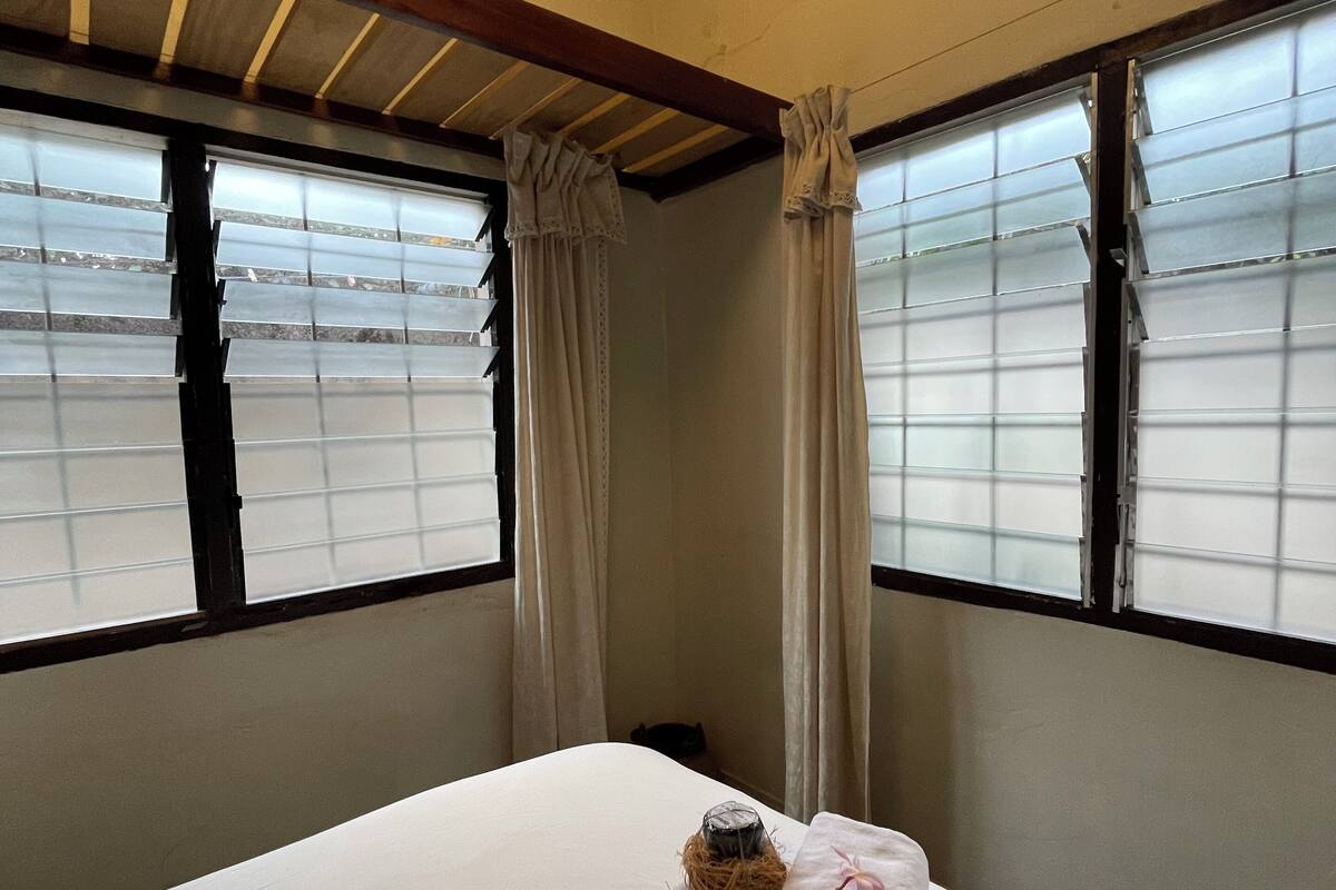 Una habitación de hotel con cama, ventana con persianas, ventilador de techo y aire acondicionado.