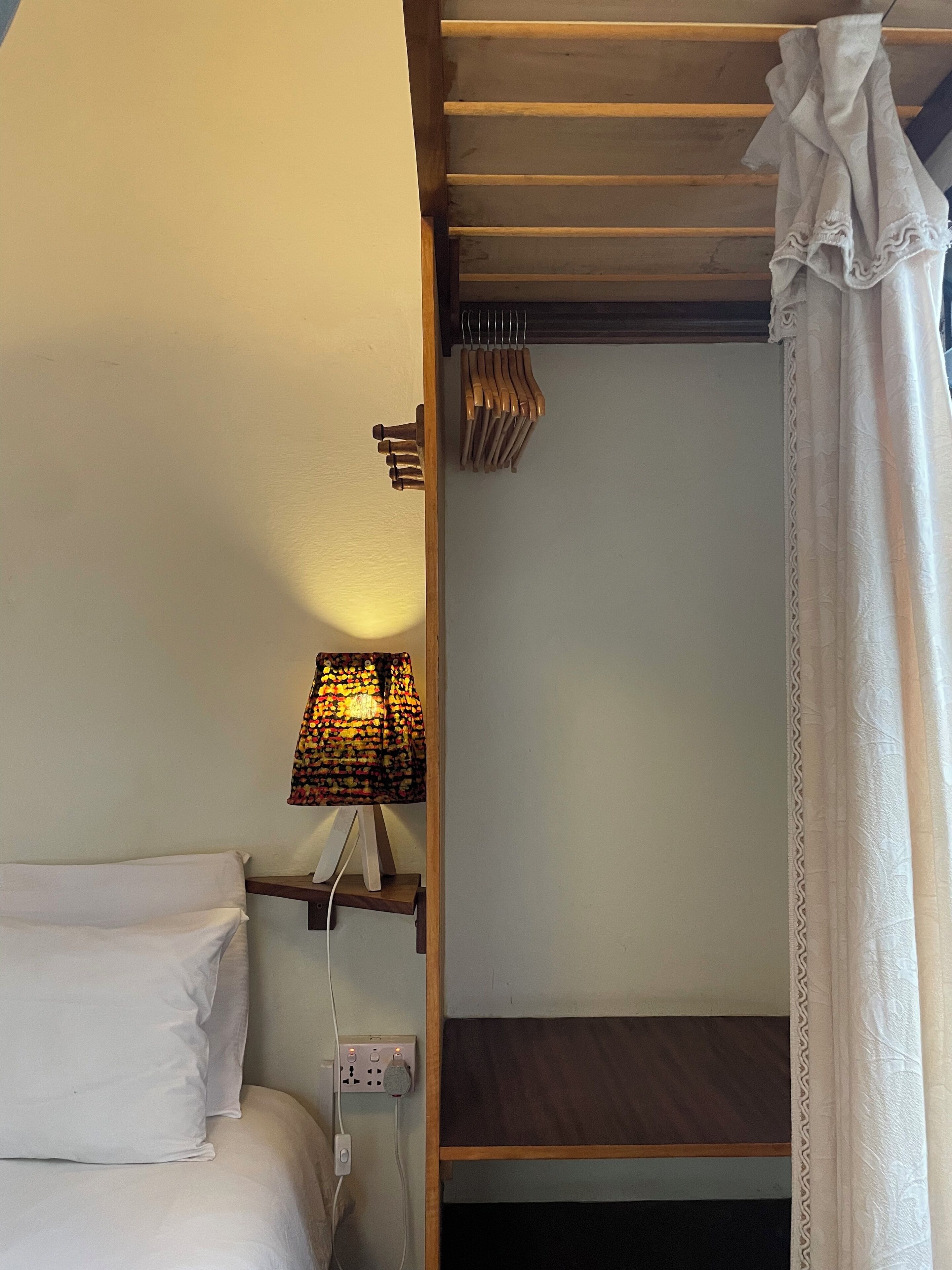 A small, compact room with a bed, a bedside table, a lamp, and a curtain.