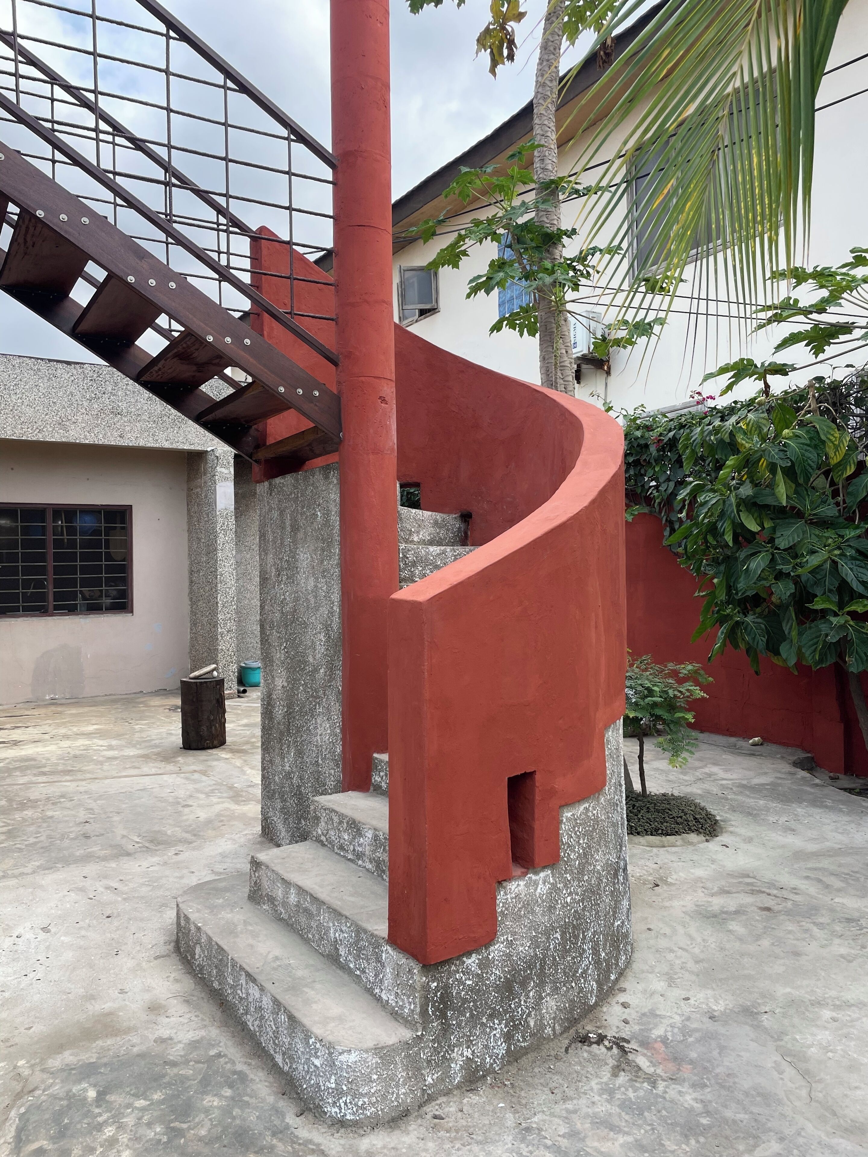 Una escalera de caracol con detalles rojos y barandilla metálica, que conduce a un nivel superior.