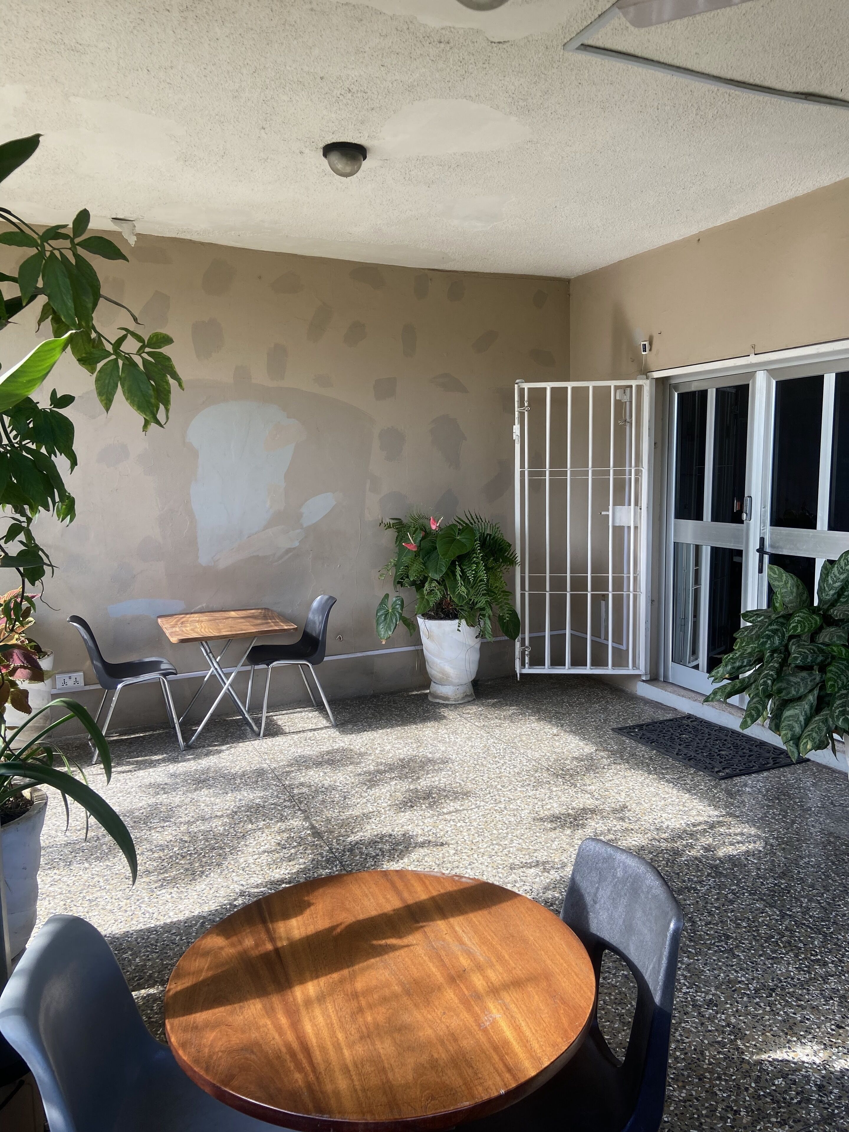 A covered patio area with a round wooden table and chairs, a potted plant, and a sliding glass door.